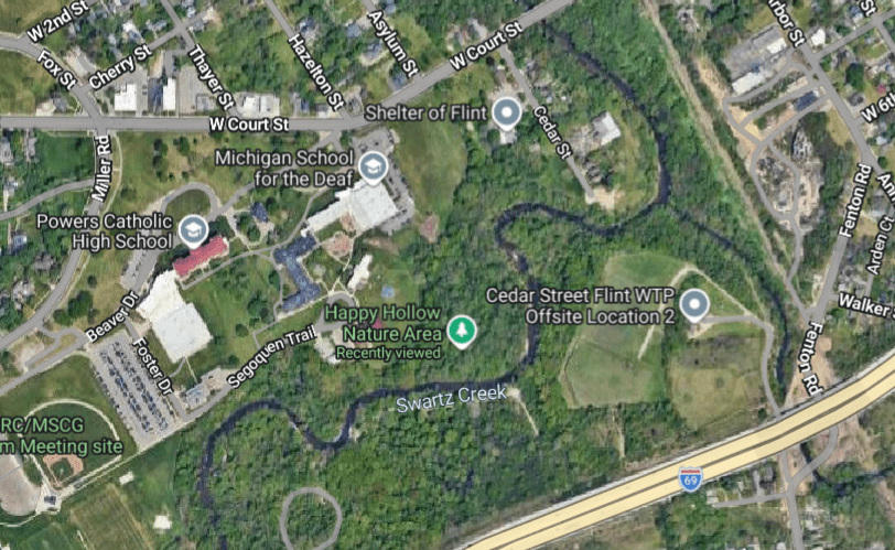Aerial view of a neighborhood featuring several landmarks including Powers Catholic High School, Michigan School for the Deaf, and the Shelter of Flint, alongside Swartz Creek and nearby nature areas.